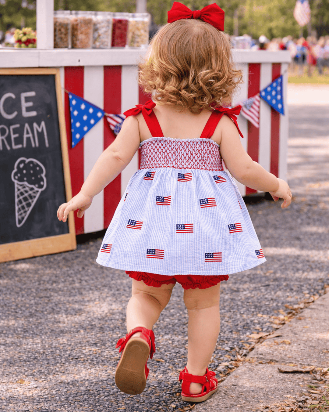 Child in a patriotic dress walking towards an ice cream stand with American flags.