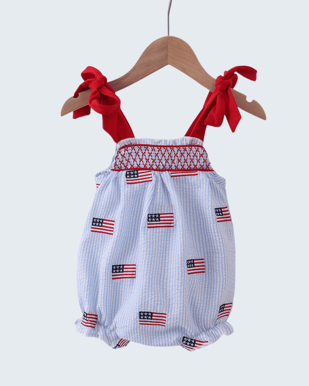 Baby romper with American flag pattern on a hanger against a white background