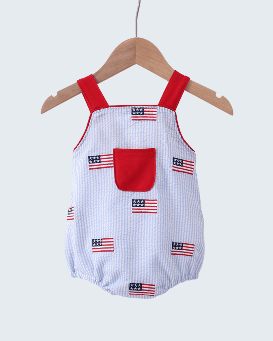 Baby romper with American flag pattern on a hanger against a light gray background