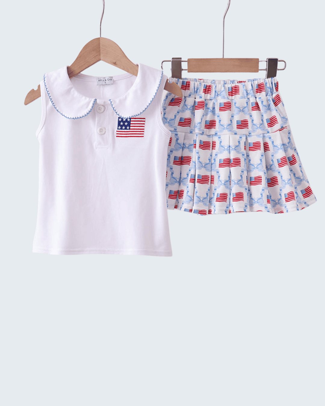 Children's outfit with white top and patterned shorts on hangers against a white background