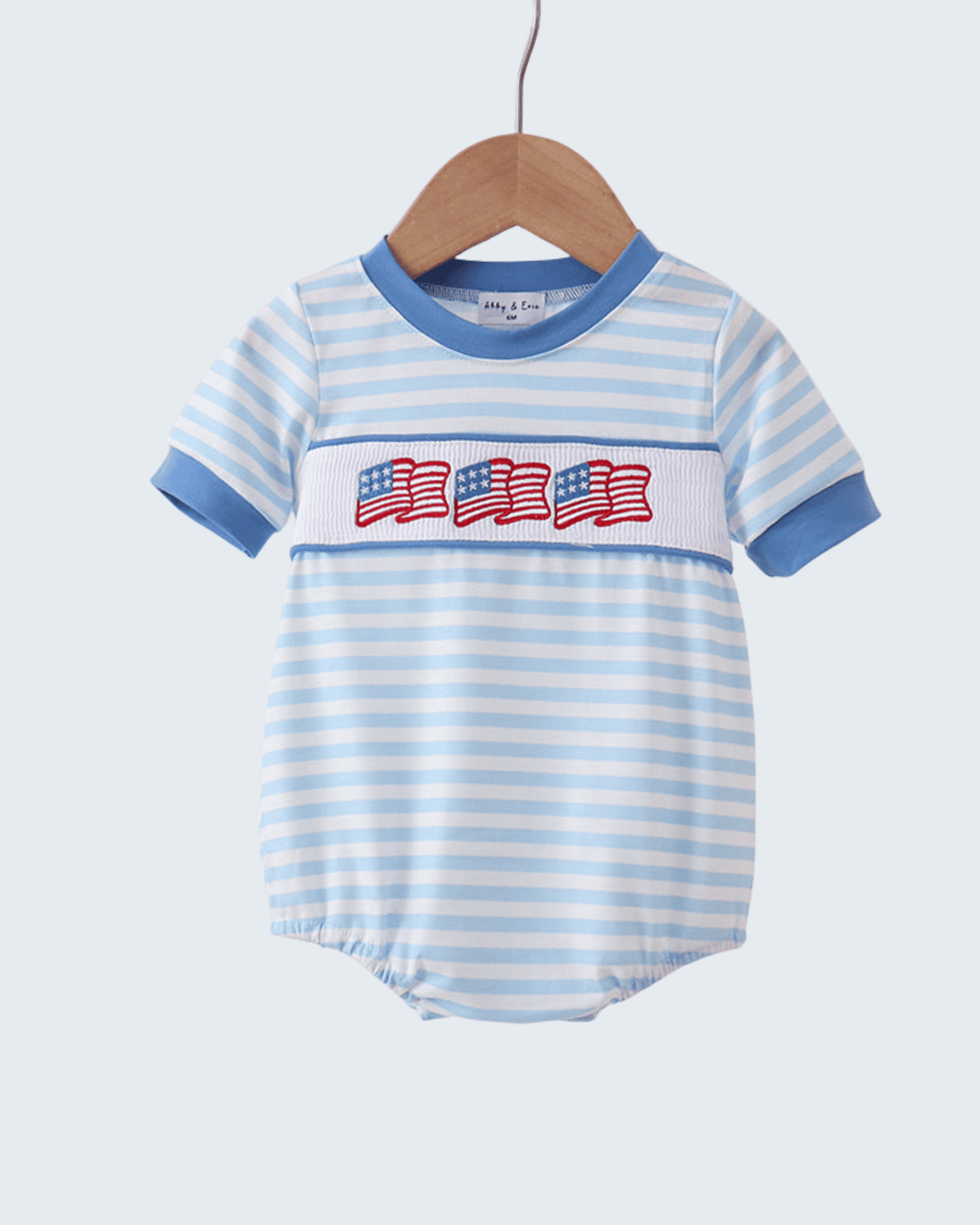 Baby romper with blue and white stripes and American flag design on a hanger against a light gray background.