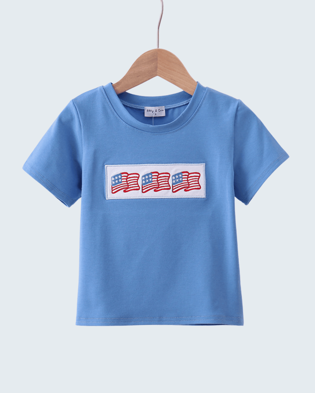 Blue t-shirt with American flag design on a hanger against a light gray background