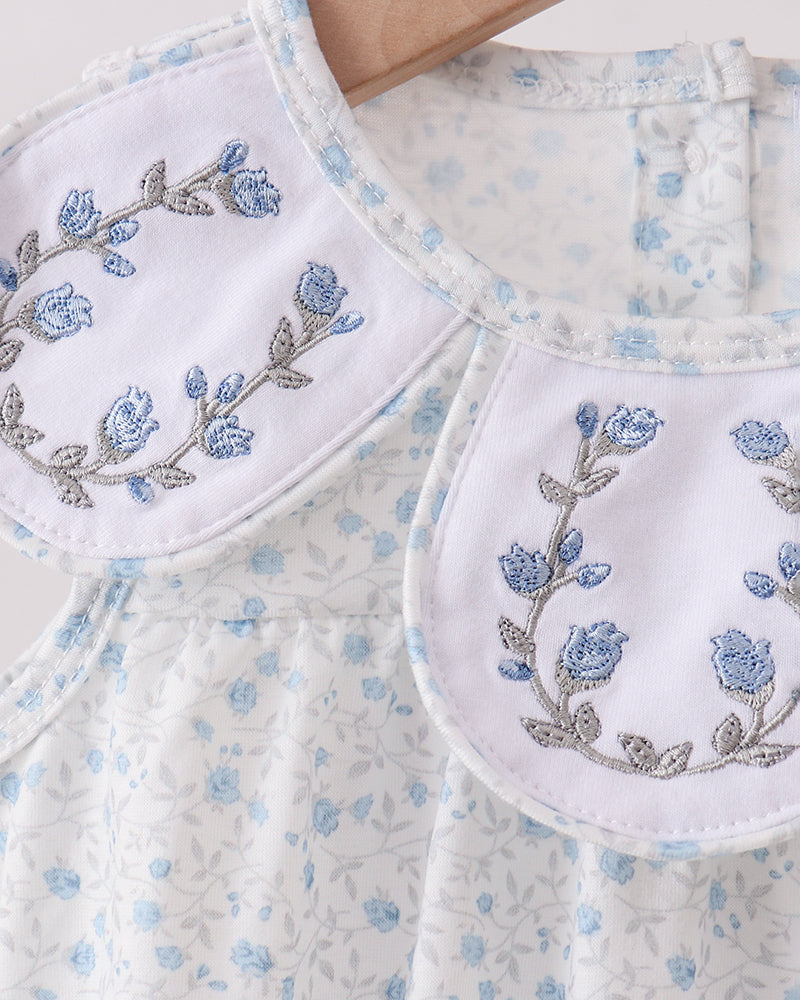 Embroidered floral design on a white garment with blue flowers.