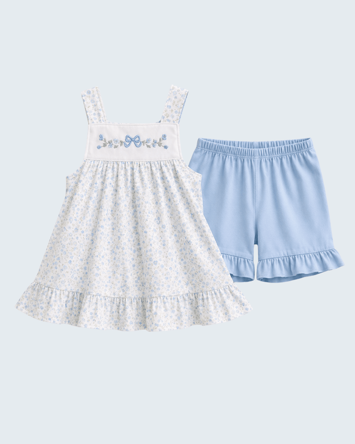 White dress with floral embroidery and blue shorts on a light gray background