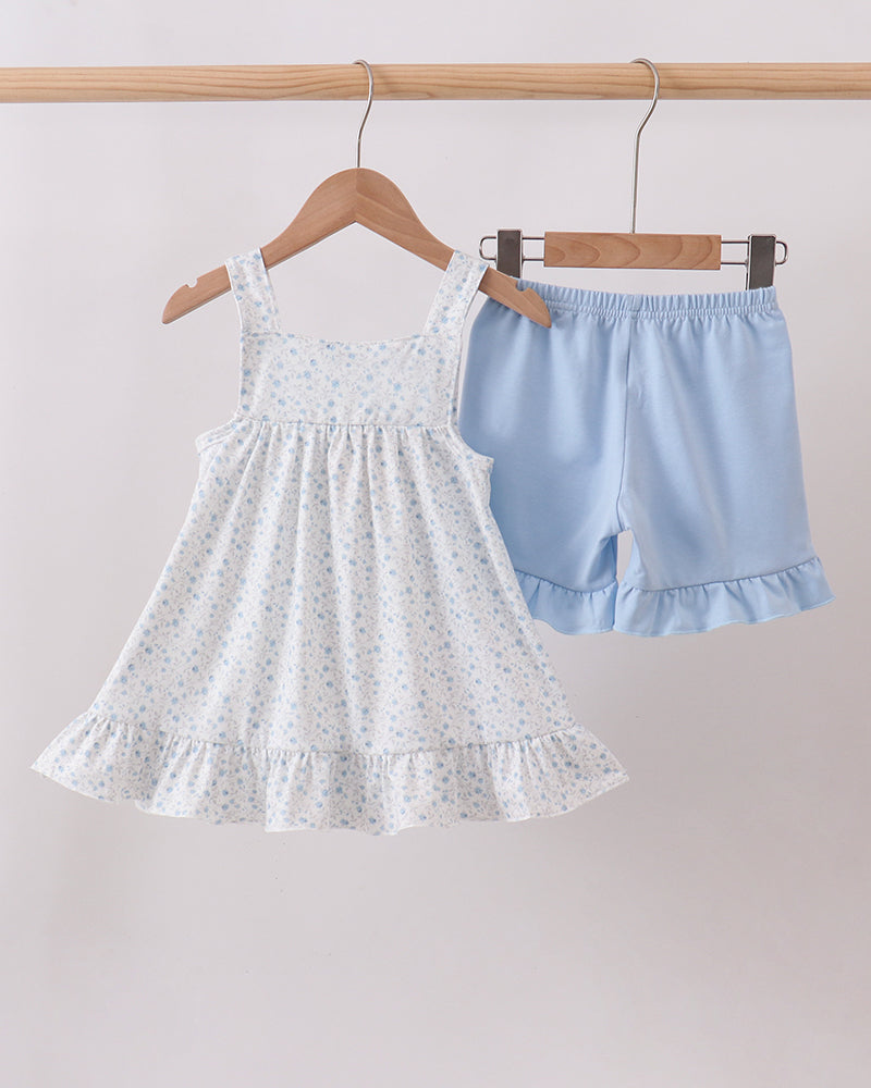 White dress and blue shorts on hangers against a light gray background
