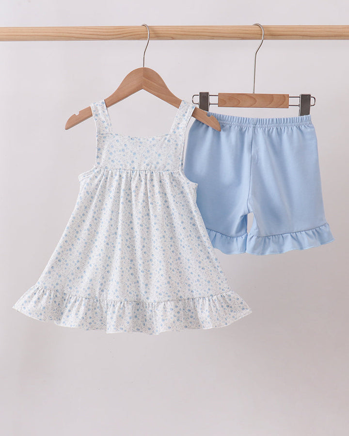 White dress and blue shorts on hangers against a light gray background