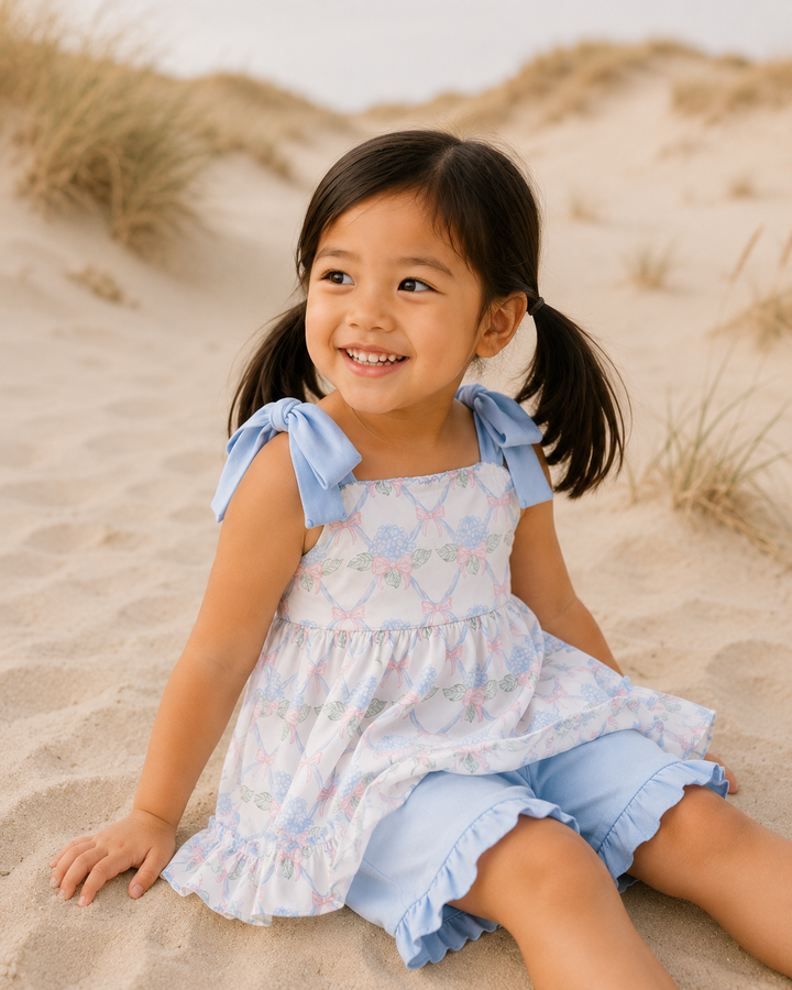 Young girl in a floral dress with blue accents sitting on sand dunes.