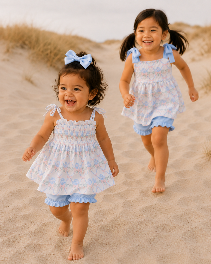 Two young girls in matching dresses running on a sandy beach.