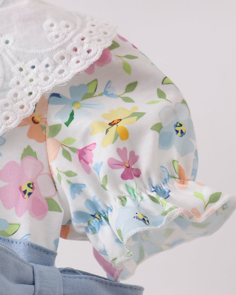 Floral baby romper with a white lace trim and blue bow on a light gray background