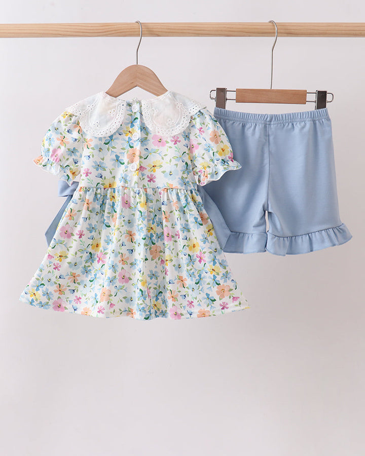 Floral dress and blue shorts on hangers against a plain background
