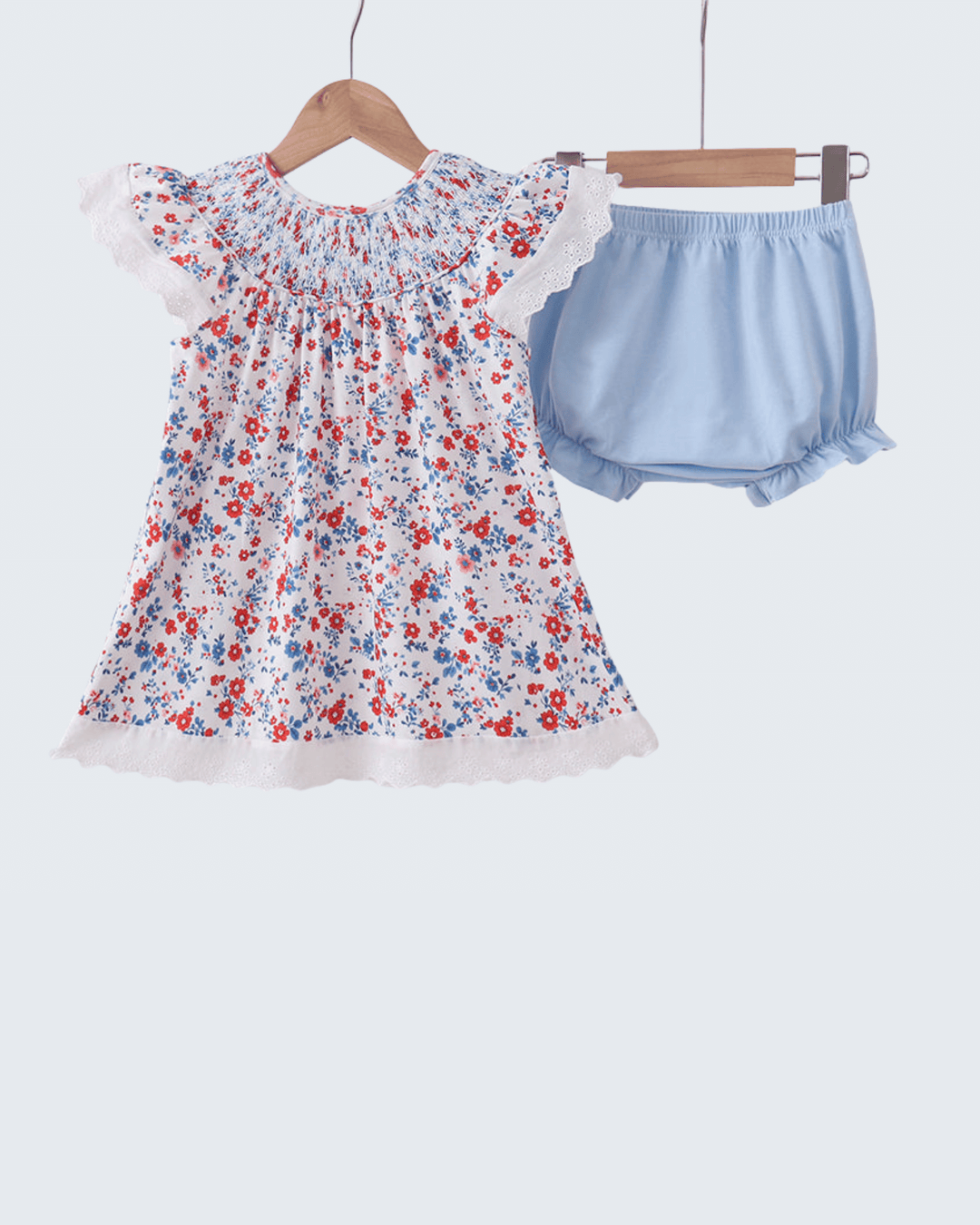 Floral dress and blue bloomers on hangers against a white background