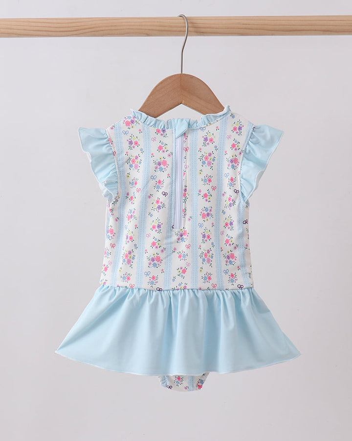 Light blue swimsuit with floral pattern on a wooden hanger against a plain background