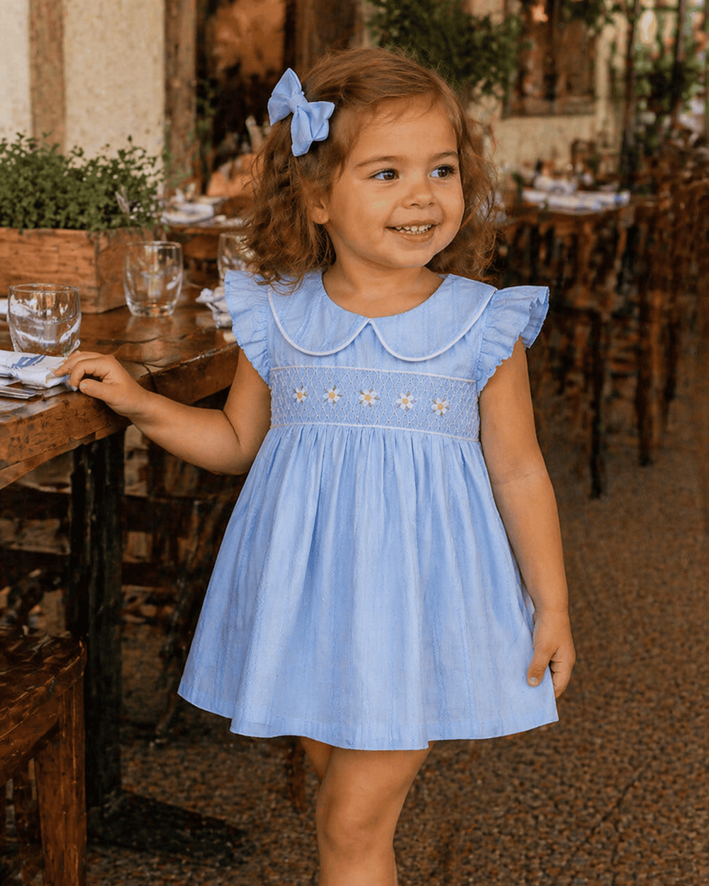 Young girl in a blue dress with star patterns standing in a restaurant setting.
