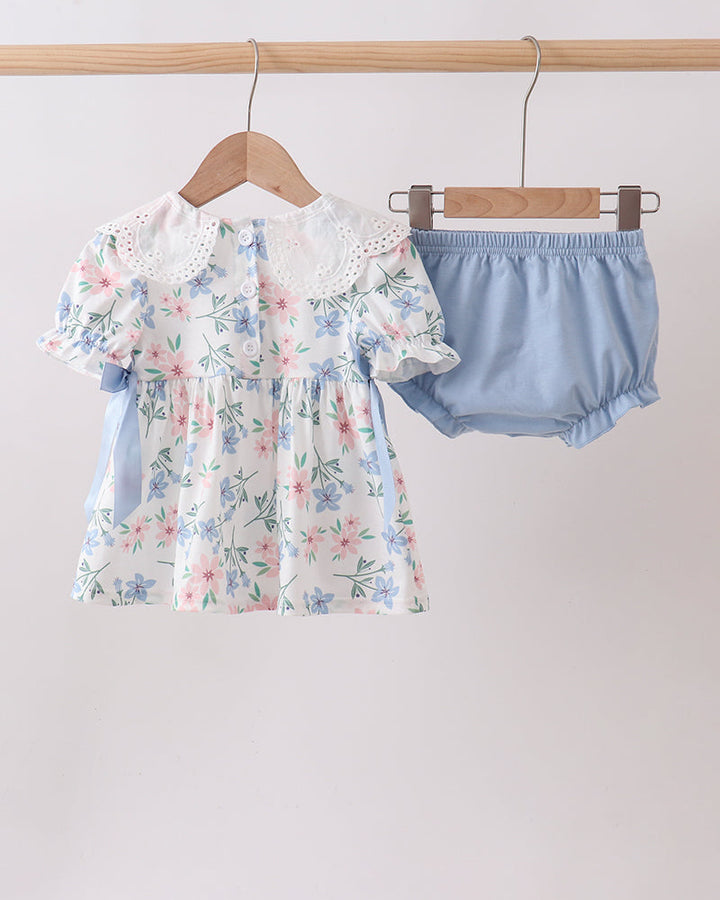 Floral dress and blue bloomers on hangers against a light gray background
