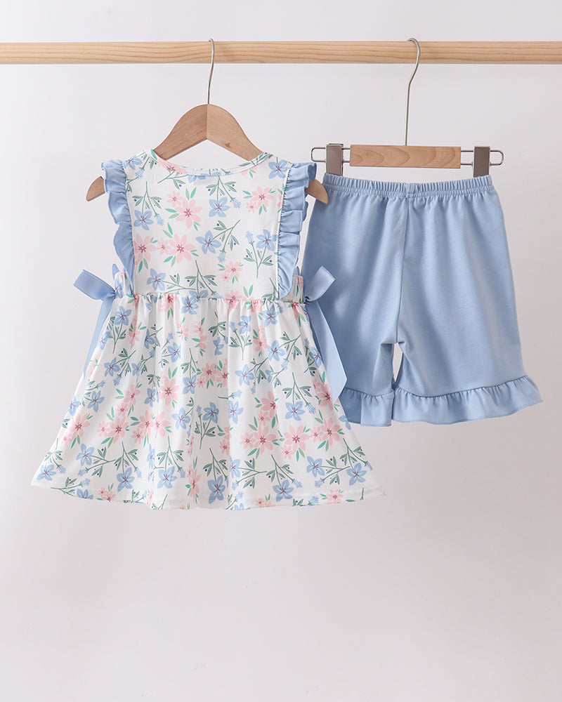 Floral dress and blue shorts set on hangers against a white background