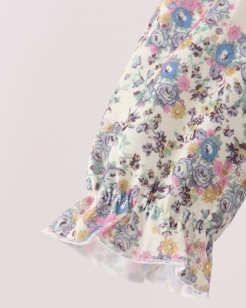 Close-up of a floral-patterned blouse sleeve with puff sleeves and a ruffled hem, featuring a cream base with blue, pink, yellow, and purple flowers.