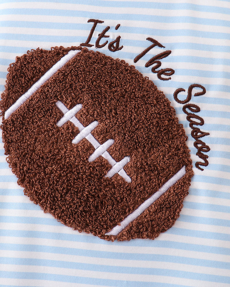 Close-up of a baby garment with light blue and white horizontal stripes, featuring a large brown football applique with white laces and the phrase &