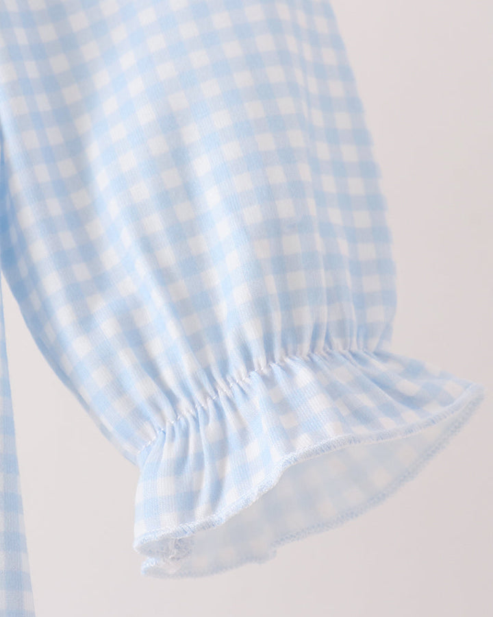 Close-up of a light blue and white gingham fabric sleeve with a gathered ruffled cuff, shown against a plain light background.