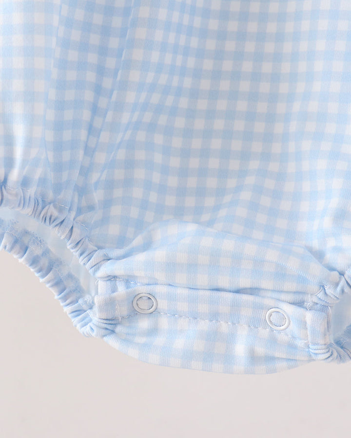 Close-up of a baby romper or bodysuit fabric in a light blue and white gingham check pattern, showing the elastic leg cuffs and snap closures.