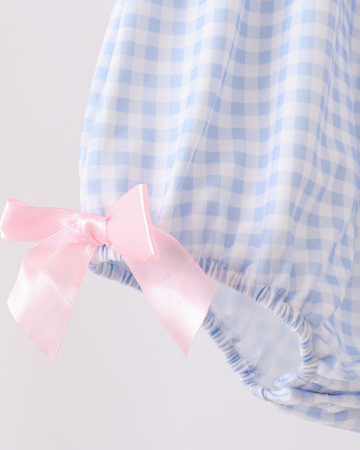 Blue gingham romper with large pink bow at neckline and ruched blue trim.