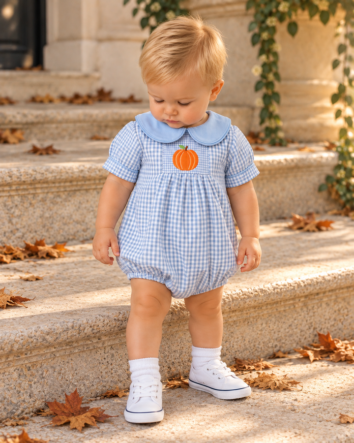Child wearing light blue gingham romper with orange pumpkin embroidery and blue collar
