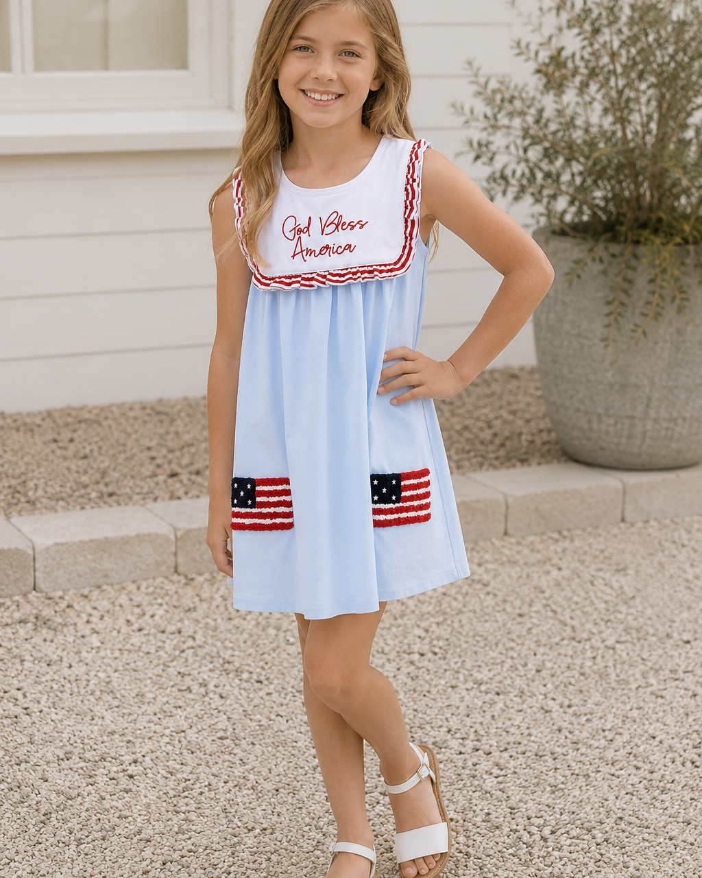 Young girl wearing a light blue dress with red and white accents, standing outdoors.