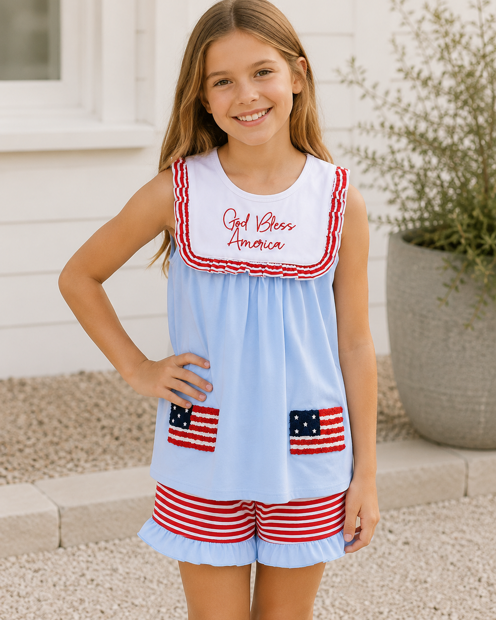 Young girl wearing a light blue dress with red and white accents and American flag designs, standing outdoors.