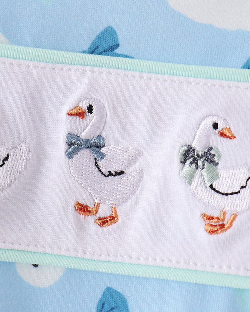 White-and-blue goose embroidery detail on light fabric leg of romper.