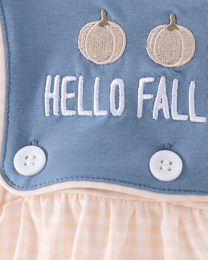 Close-up of a baby outfit featuring a dusty blue bib with &