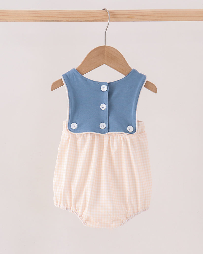 A baby romper hanging on a wooden hanger against a light beige background. The romper features a dusty blue sleeveless bodice with snap buttons and a pale peach-and-white gingham patterned bottom.