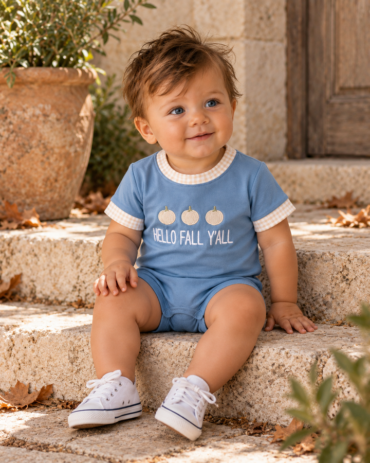 A baby sitting on outdoor stone steps wearing a light blue short-sleeve romper with white trim and a &