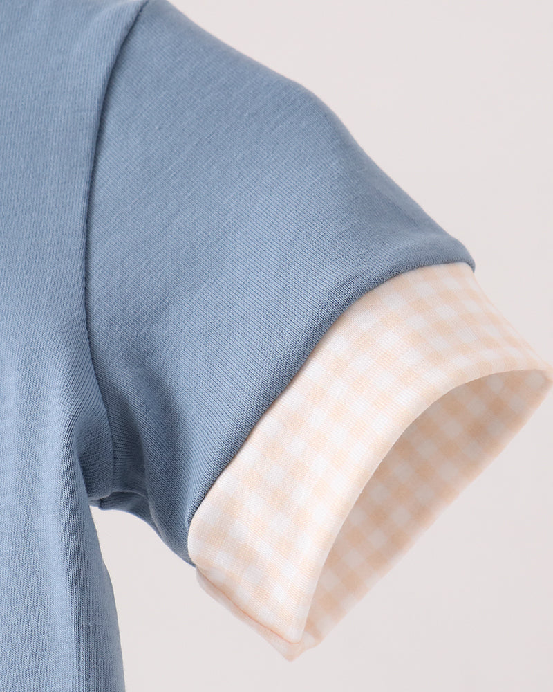 Close-up of a short-sleeve top showing a light blue ribbed fabric sleeve with a turned-up cuff revealing a pale peach and white gingham lining.