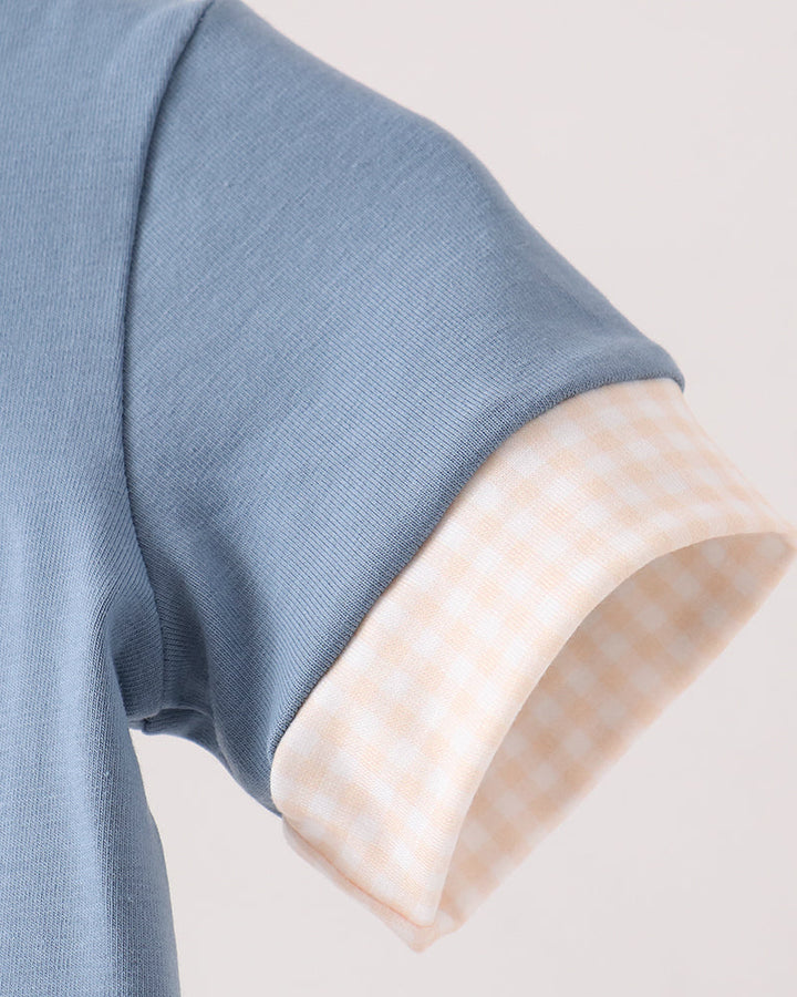Close-up of a short-sleeve top showing a light blue ribbed fabric sleeve with a turned-up cuff revealing a pale peach and white gingham lining.