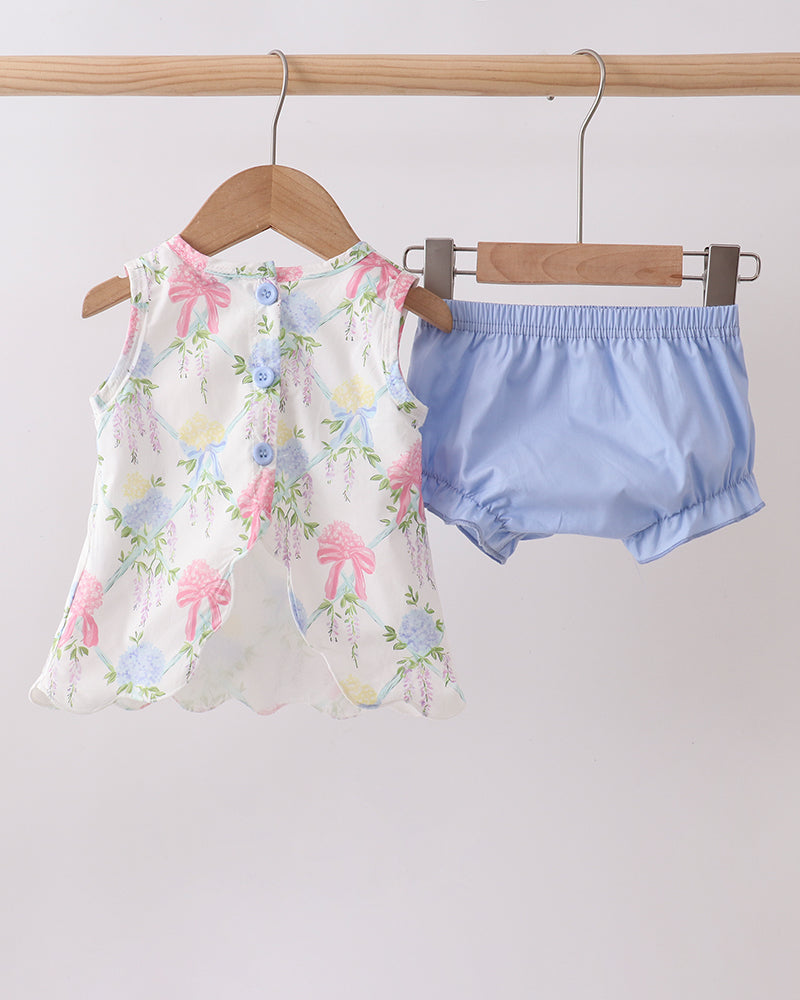 Floral top and blue shorts hanging on wooden hangers against a white background