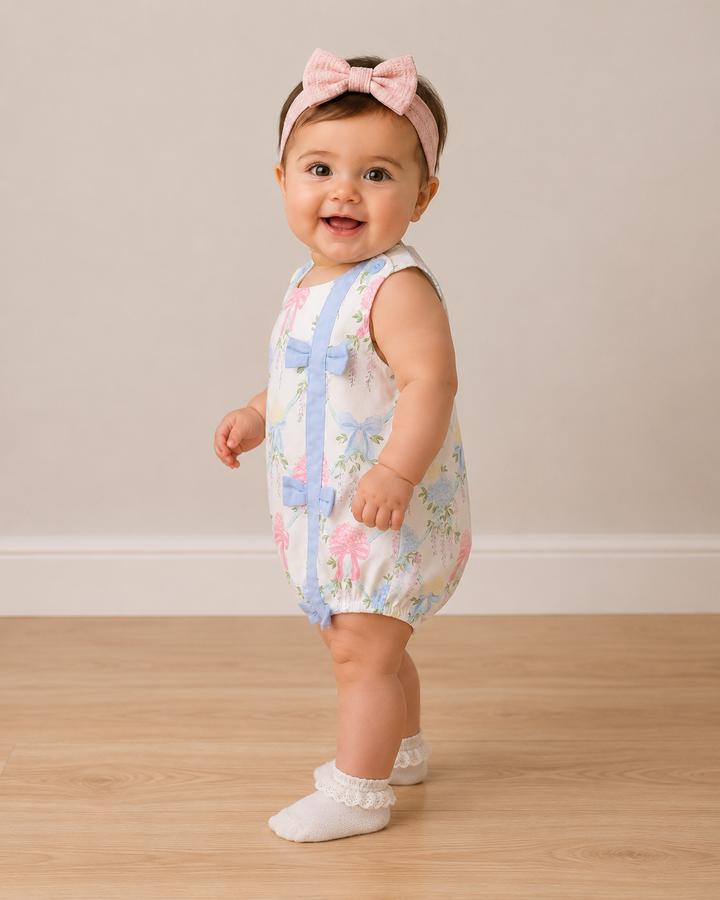 Baby wearing a floral romper with blue accents on a wooden floor.