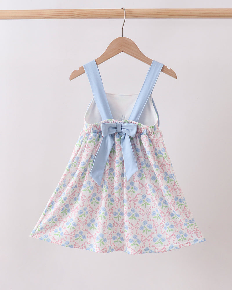 Floral dress with blue straps on a wooden hanger against a white background