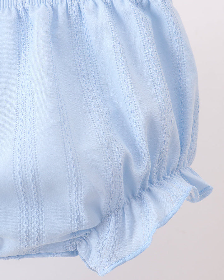 Close-up of light blue ruffled fabric with vertical eyelet embroidery, likely a baby bloomers or diaper cover detail, on a plain light background.