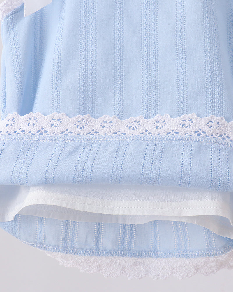 Close-up of a light blue embroidered fabric garment with white lace trim and a white inner layer, shown against a pale gray background.