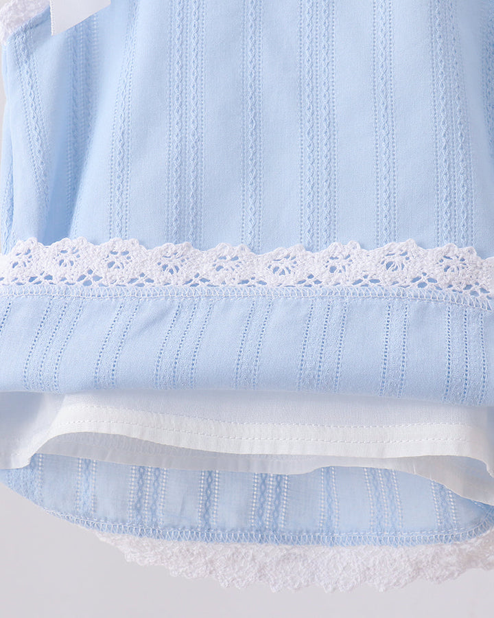 Close-up of a light blue embroidered fabric garment with white lace trim and a white inner layer, shown against a pale gray background.