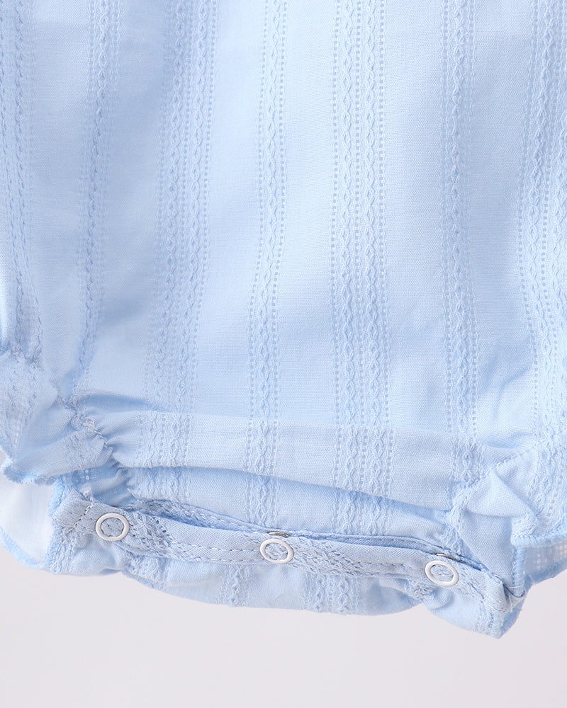 Close-up of a light blue baby romper or bodysuit showing the bottom hem with three white snap buttons and a textured vertical stripe pattern.