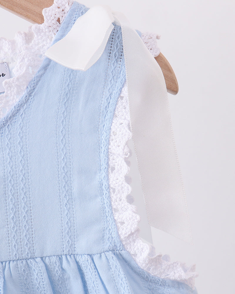 A close-up of a light blue sleeveless dress with white lace trim and a white ribbon bow, hanging on a wooden hanger against a plain light background.