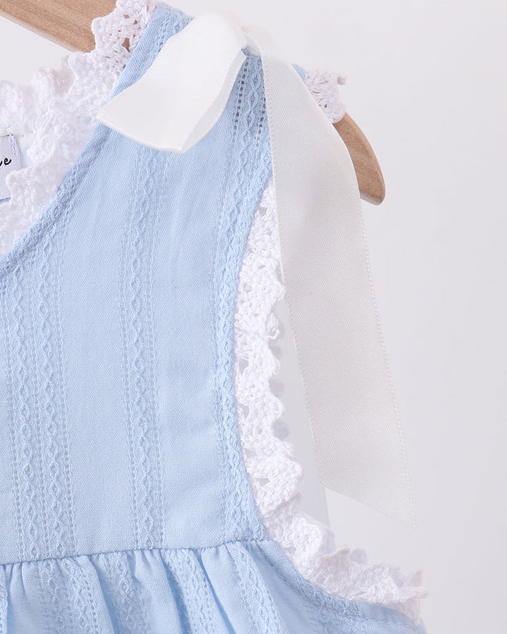 A close-up of a light blue sleeveless dress with white lace trim and a white ribbon bow, hanging on a wooden hanger against a plain light background.