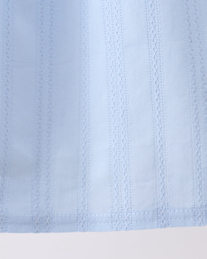 A close-up of a light blue fabric with vertical eyelet embroidery and a stitched hem, shown against a plain white background.