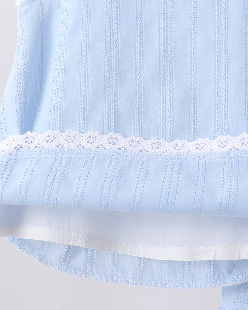 Close-up of a light blue sleeveless top with vertical eyelet embroidery, a white lace band across the chest, and a layered ruffled hem.