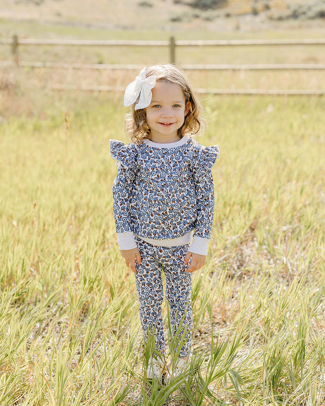 Blue floral ruffle top and matching pants set on toddler girl standing outdoors