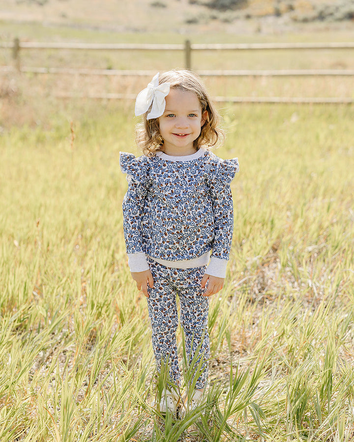 Blue floral ruffle top and matching pants set on toddler girl standing outdoors