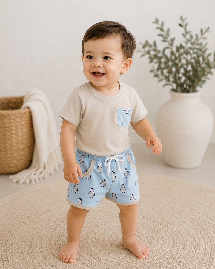 Baby wearing a beige shirt and blue shorts with animal print, standing on a beige carpet.