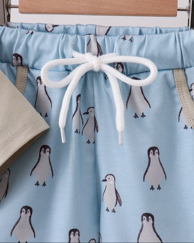 Blue shorts with penguin pattern on a hanger against a white background