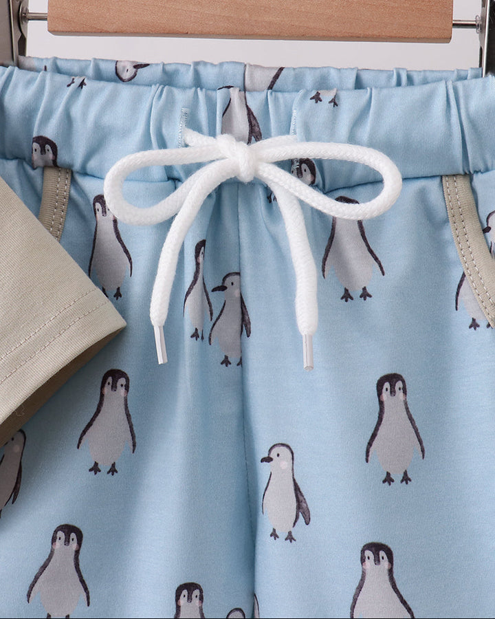 Blue shorts with penguin pattern on a hanger against a white background