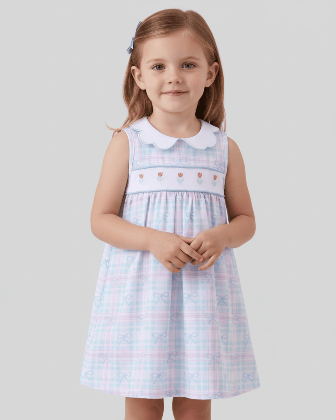 Young girl wearing a checkered dress with a white collar on a light gray background